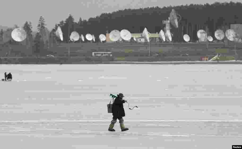 A fisherman walks on the frozen surface of a lake, with satellite dishes of a local space communication center seen in the background, in the town of Zheleznogorsk, Russia. (Reuters/Ilya Naymushin)