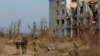 Russian servicemen walk past a destroyed residential building in the settlement of Pisky in a Russian-occupied part of Ukraine's Donetsk region. 