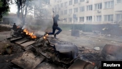 A masked man jumps over a burning barricade in front of police headquarters in the embattled southeastern port city of Mariupol on May 9.