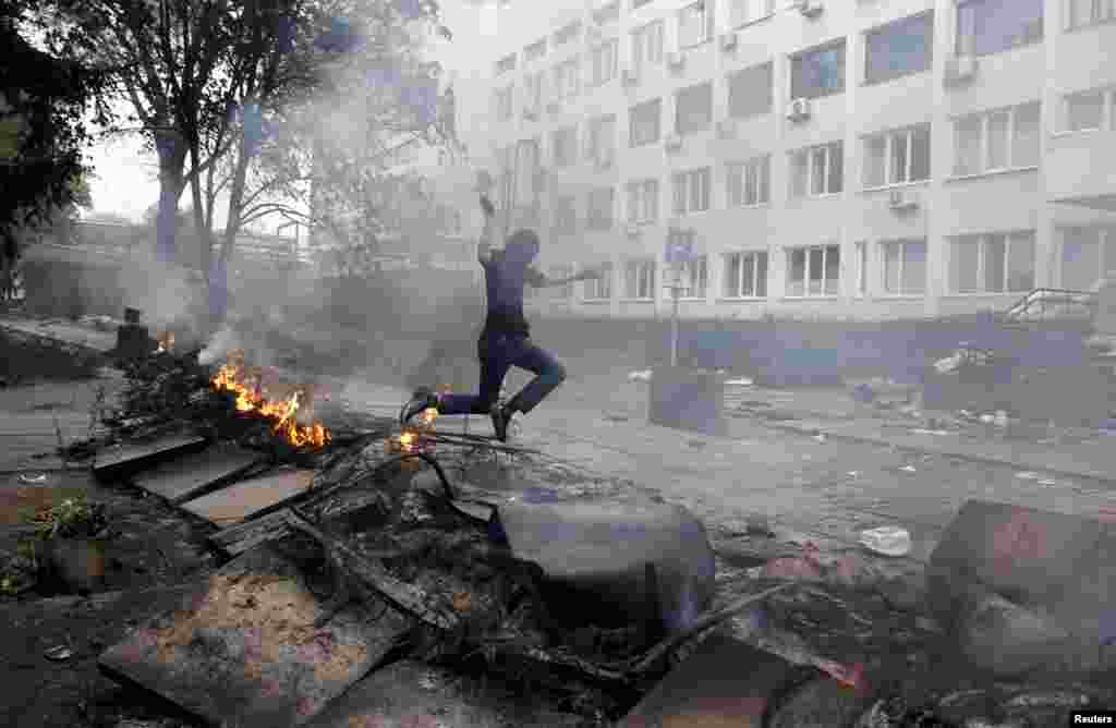 Un bărbat mascat sare peste o baricadă în flăcări în centrul orașului Mariupol pe 9 mai 2014. La începutul lunii mai, au început să se audă împușcături sporadice. În centrul orașului domnea fărădelegea, iar loialitatea în rândul forțelor de ordine locale părea incertă.&nbsp; &nbsp;