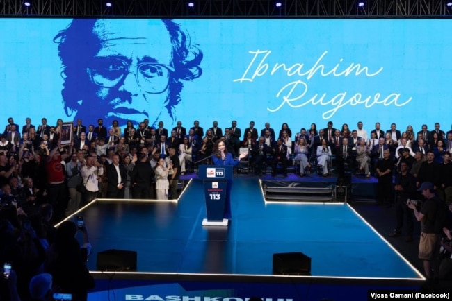 Vjosa Osmani, gjatë fjalimit në eventin hapës të fushatës zgjedhore për LDK-në. Në prapavijë, një foto dhe emri i Ibrahim Rugovës.