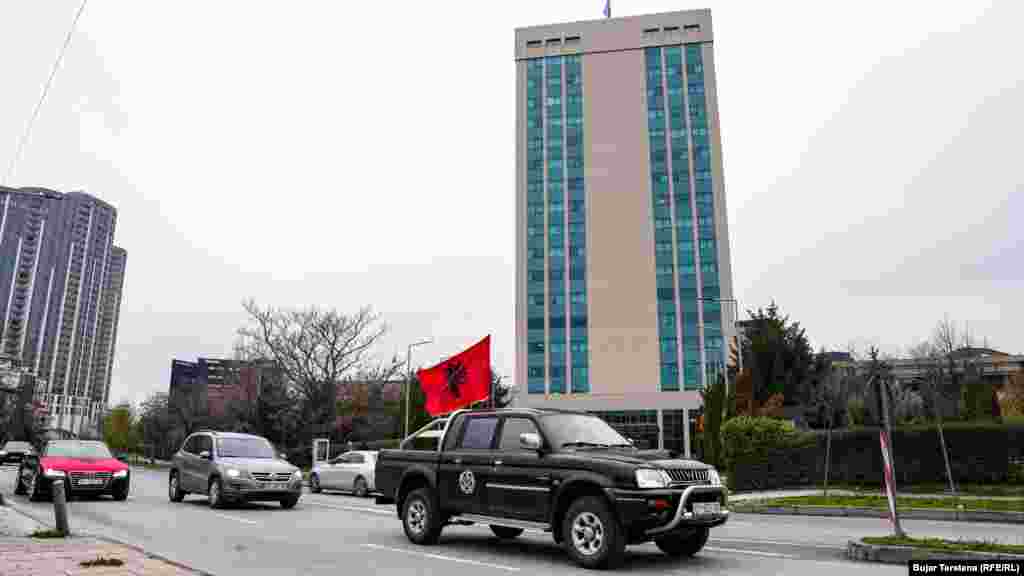 Një makinë me flamurin kombëtar shqiptar kalon pranë ndërtesës ku ndodhen disa ministri.