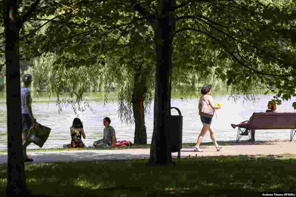 Oameni se răcoresc lângă lacul din Parcul Alexandru Ioan Cuza din București, pe fondul temperaturilor extrem de ridicate.