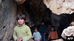 Syrian children, who evacuated their home due to shelling by regime forces, stand at the entrance of a cave in which they refuge in Ain al-Zarka northeast of Syria.