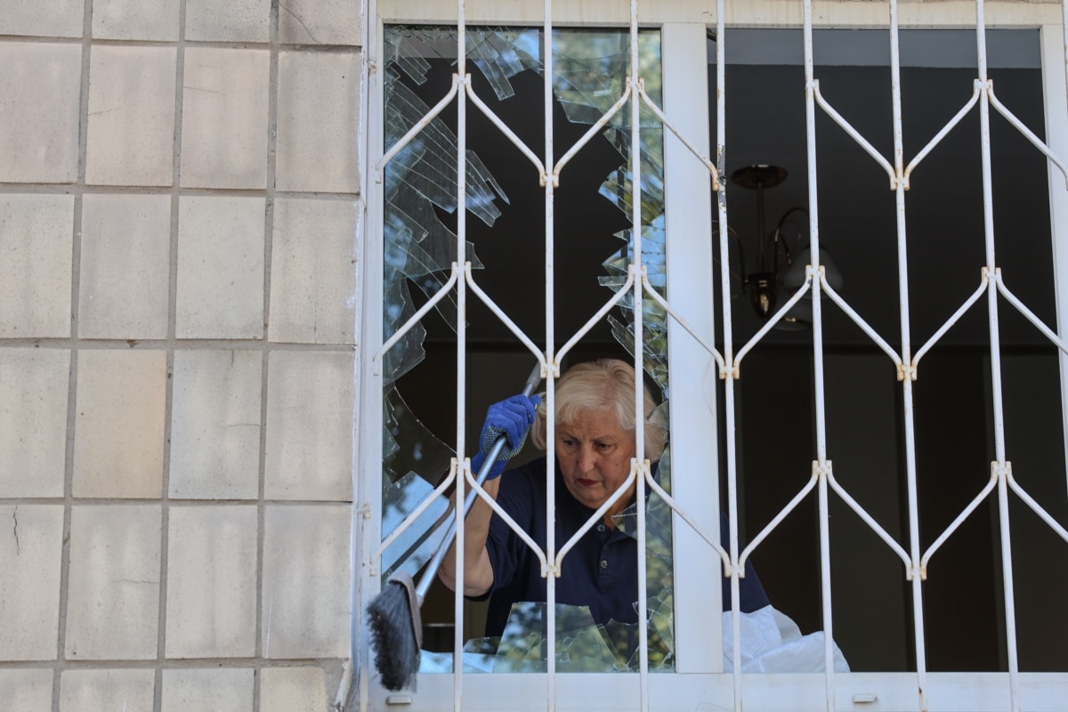 Жінка прибирає уламки скла з вікна, яке вибило вибуховою хвилею під час російського ракетного удару по Києву