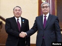 Исполняющий обязанности президента Казахстана Касым-Жомарт Токаев (справа) пожимает руку своему предшественнику Нурсултану Назарбаеву во время совместного заседания палат парламента в Астане, Казахстан, 20 марта 2019 года.