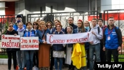A belorusz Tut.by oldal újságírói „Nem tüntetek, hanem dolgozom” (balra), „Ez vagyok én munka közben” (középen) és „Szabadságot az újságíróknak!” feliratú transzparenseket tartanak egy minszki rendőrőrs előtt 2020 szeptemberében kollégáik letartóztatása ellen tiltakozva