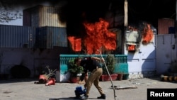 Поліцейський забирає речі перед контрольно-пропускним пунктом, підпаленим протестувальниками біля консульства США у Карачі, Пакистан, 1 березня 2026 року