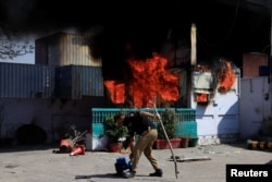 Полицай пред оградата на американското консулство в Карачи, подпалена от протестиращи срещу САЩ, 1 март 2026 г.