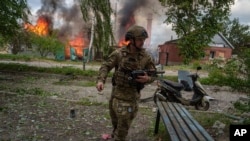 Украинский полицейский на фоне горящего дома, разрушенного российским авиаударом в Волчанске, Харьковская область, 11 мая 2024 года
