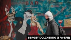Мужчина в защитной маске проходит мимо стены с уличной рекламой в Киеве, Украина, 22 апреля 2020 года.