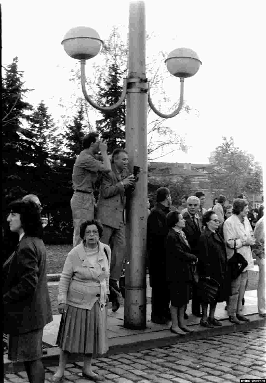 Двама от фотографите, снимали шествието на &quot;Екогласност&quot; на 3 ноември 1989 г. Усмихнатият вдясно е Стефан Тихов. Много хора не взимат участие в шествието, а го наблюдават отстрани. Осветителните тела на площада са монтирани през 80-те години.