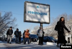 Қазақстан Конституциясы жөнінде референдум өтетіні туралы көшедегі жарнаманың қасынан өтіп жатқан адамдар. Алматы, 12 наурыз, 2026 жыл.