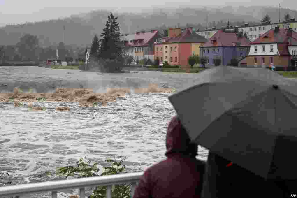 Ljudi sa kišobranima gledaju bujicu vode sa mosta preko rijeke Biala u Glucholazyju, na jugu Poljske, 14. septembra 2024.