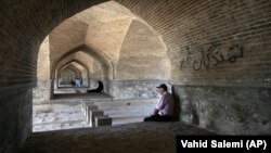 In this Tuesday, July 10, 2018 photo, people rest under an arch of the 400-year-old Si-o-seh Pol bridge, named for its 33 arches, that now spans a dried up Zayandeh Roud river, in Isfahan, Iran.