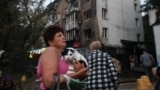 Жінка тримає свого собаку, разом з яким покинула пошкоджений російською атакою будинок