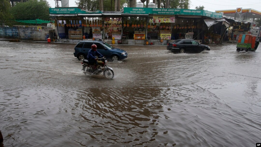 A motorcycle and cars drive through a flooded road caused by heavy rain in Peshawar on April 15.