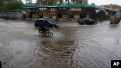 A motorcycle and cars drive through a flooded road caused by heavy rain in Peshawar on April 15.