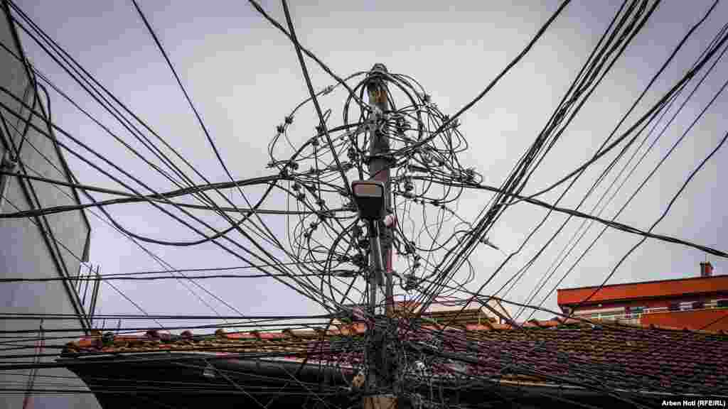 Tela të rrymës, kabllo të shumta telefonike, interneti e të tjera, në një shtyllë betoni që pothuajse mbulojnë kulmin e një shtëpie në lagjen "Vellusha" në kryeqytet. 