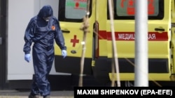 Медик в защитном костюме рядом с машиной скорой помощи на территории больницы для пациентов с коронавирусом в Подмосковье. 