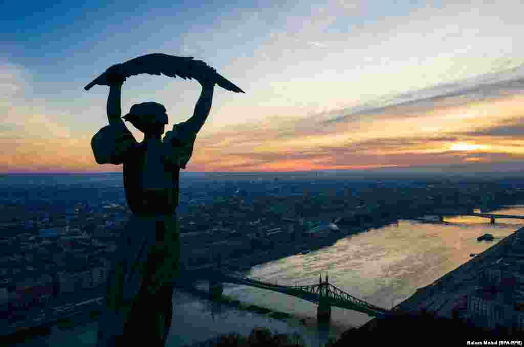 Солнце встает за статуей Свободы на вершине горы Геллерт в Будапеште. (epa-EFE/Балаш Мохай)