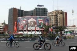 Велосипедисти проїжджають повз білборд із портретом убитого верховного лідера Ірану, аята́лли Алі Хаме́неї, на площі Валіаср у Тегерані 22 березня 2026 року