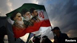 A man holds a flag featuring late leader of the Islamic Revolution Ayatollah Ruhollah Khomeini, late Supreme Leader of Iran Ayatollah Ali Khamenei, and Iran's new Supreme Leader Mojtaba Khamenei, at a rally in Tehran on April 29. 