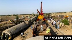 Workers clear the wreckage from a railroad track in Sindh Province on June 8, a day after a packed inter-city train ploughed into another express train that had derailed.