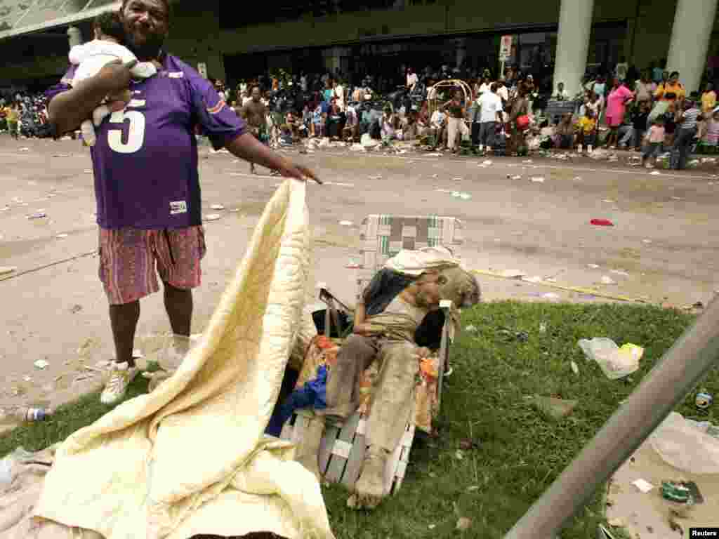 A man holding a baby uncovers the body of a dead man, suspected to have been sitting there for two days, outside the New Orleans Convention Center September 1, 2005. Several people among the thousands of stranded hurricane evacuees have died while waiting outside the building, with no sign of imminent help on the way. REUTERS/Rick Wilking 