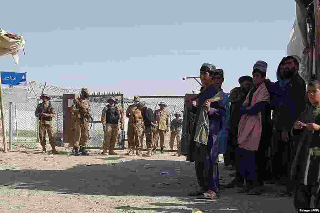 Пакистанские солдаты стоят на страже, а афганцы, оказавшиеся в затруднительном положении, ждут открытия пункта пересечения границы 12 августа