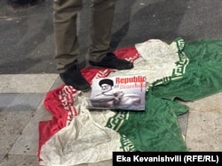 თბილისში, ირანის საელჩოსთან გამართულ საპროტესტო აქციაზე ფეხით თელავენ აიათოლა ალი ხამენეის პლაკატს და ირანის დროშას.