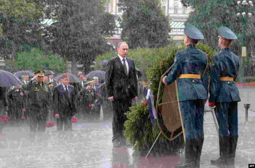 Президент России Владимир Путин стоит под дождем во время траурной церемонии в Москве в 76-ю годовщину нападения нацистов на СССР. Утром 22 июня погода в Москве была переменчивой, вспоминает фотограф Алексей Дружинин. Однако когда он приехал в Вечному огню, небо прояснилось и казалось, что &laquo;погода будет солнечной весь день&raquo;, вспоминает он. Фотограф, работающий для администрации президента, рассказал: когда делегация подошла к венку, &laquo;дождь полил стеной &ndash; как из ведра&raquo; и продолжался все 15 минут, что длилась церемония с участием президента. Снимок получил известность, однако автор считает, что его роль в этом невелика: &laquo;Реакция была не на саму фотографию, а на ситуацию, когда Путин отказался от зонта и в знак траура стоял под проливным дождем&raquo;. Позднее, когда Путина спросили об отсутствии зонта, тот ответил в духе тщательного поддерживаемого им образа &laquo;крутого парня&raquo;: &laquo;Не сахарный, не растаю&raquo;