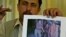 Saddam Saleh, a former prisoner at Abu Ghraib, shows a photograph at a 2004 press conference from the scandal that includes him in the middle of a group of naked prisoners being mocked by Lynndie England.