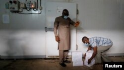 Рабочий в Гане заносит упаковки с вакциной от коронавируса в прохладное помещение.
