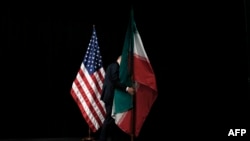 A staffer removes Iranian and US flags from the stage after a group picture with foreign ministers and representatives of Unites States, Iran, China, Russia, Britain, Germany, France and the European Union.