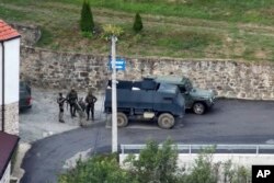 In this photo provided by the Kosovar police, a group of armed, masked men stand in front of a monastery in the northern village of Banjska. 