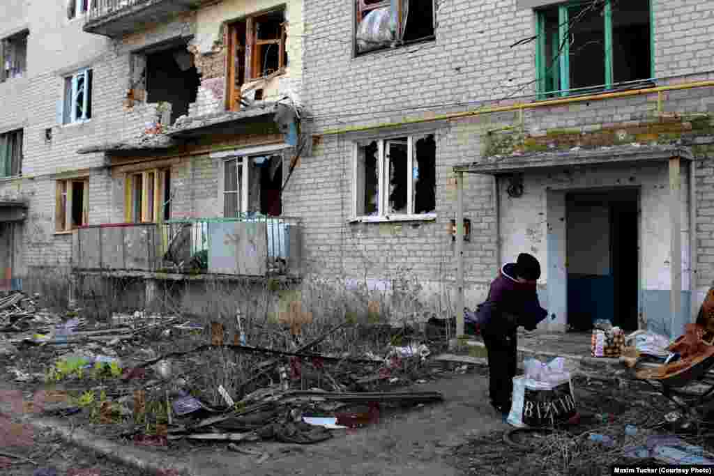 Женщина собирает вещи из заброшенного многоэтажного дома наполовину разрушенного артиллерийскими обстрелами в Песках