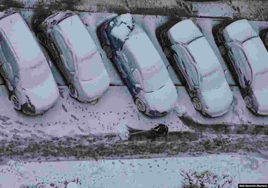 A worker cleans a street where cars are covered in snow amid the first snowfall in Kyiv on November 21.&nbsp;