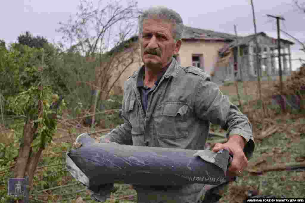In this photo made available by the Armenian Foreign Ministry, a man holds a spent artillery shell casing.