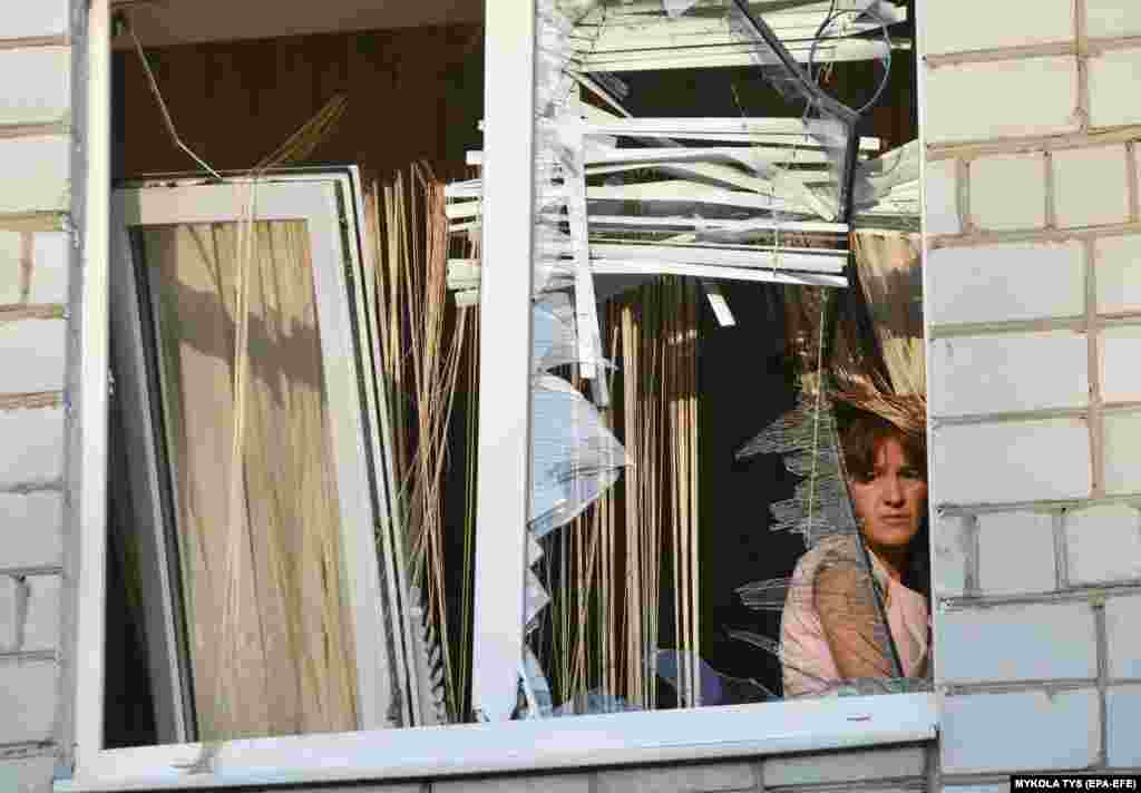 A woman looks through the broken window of her damaged apartment at the site of a combined Russian strike that hit a residential area in Lviv, western Ukraine.