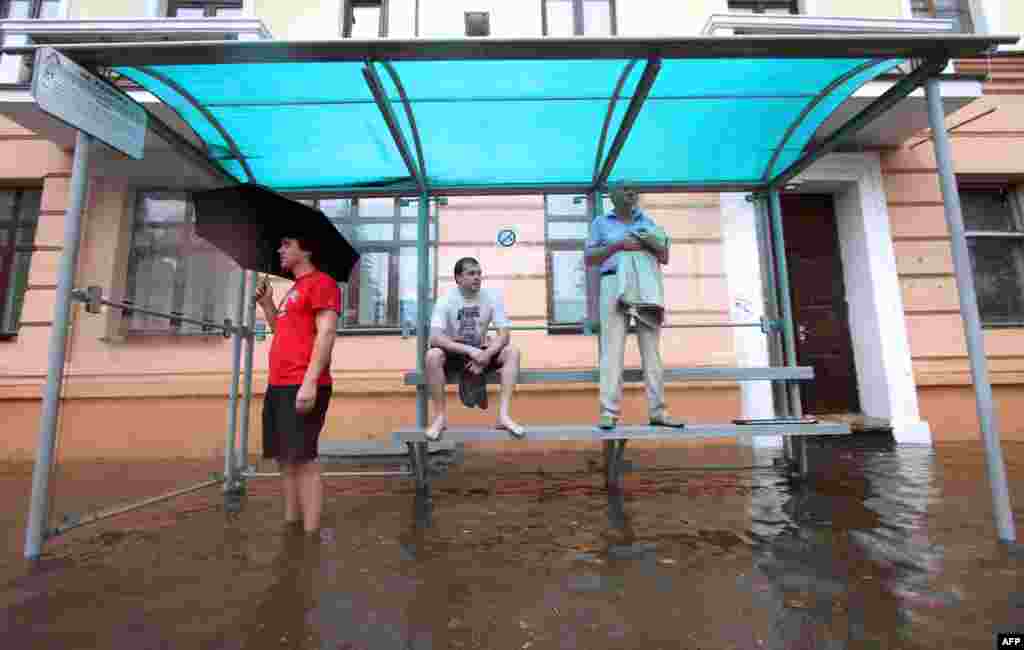 People wait for at a flooded bus stop during heavy rain in Minsk on August 12. (AFP/Sergei Gapon)