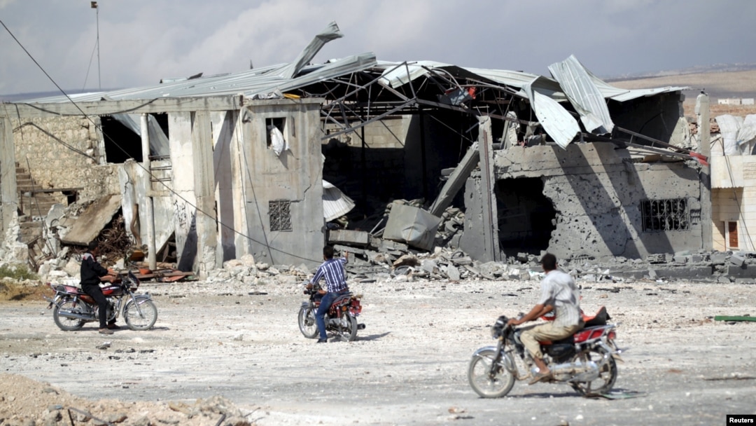 Men on motorcycles inspect a site hit by what activists said were air strikes carried out by the Russian Air Force in the southern town of Babila on October 7.