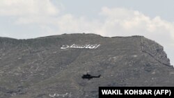 Un elicopter militar zboară pe lângă un deal pe care se poate citi „Afganistan” în limba dari. 11 mai, 2021. 