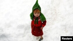 An internally displaced Afghan child stands outside her shelter during a snowfall in Kabul on February 5.