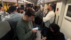 Commuters looks at their mobile phones while traveling on the subway in Tehran.