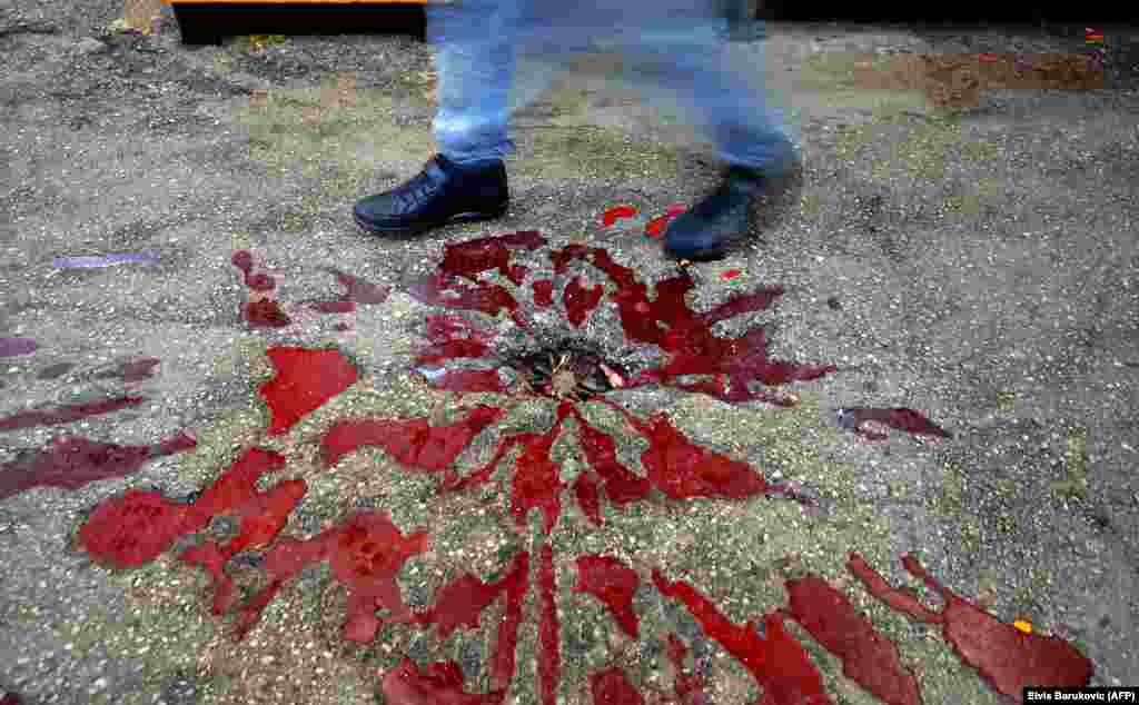 People walk by a &quot;Sarajevo rose&quot; in Sarajevo.&nbsp;They are markings of mortar shelling from the 1992-95 siege in which 10,000 people died and can be found around the city. They are the original damage scars in concrete that were accented in red paint. (AFP/Elvis Barukcic)&nbsp;