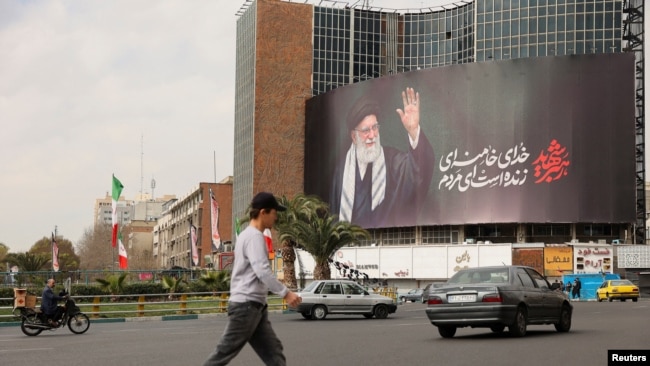 Njerëz kalojnë pranë një billboardi të ish-udhëheqësit suprem të Iranit, Ajatollah Ali Khamenein, në një rrugë, pasi ai u vra në sulme izraelite dhe amerikane, në Teheran më 2 mars.