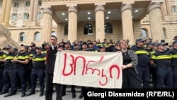 დემონსტრანტები პოლიციის კორდონის წინ დგანან ბანერით: "ცირკი" - თბილისის საქალაქო სასამართლომ ამ დღეს 21 წლის დემონსტრანტს, მათე დევიძეს, 4,5 წლით პატიმრობა მიუსაჯა. 12 ივნისი, 2025 წელი