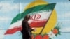 Járókelő Teherán központjában az Iszlám Köztársaság nemzeti lobogóját ábrázoló falfestmény előtt 2019. november 7-én