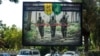 IRAQ -- A picture taken on June 20, 2018 shows a propaganda billboard for the pro-Iran Hezbollah Brigades militia hanging over Palestine Street in the centre of the Iraqi capital Baghdad, depicting three of their masked fighters walking along a road betwe